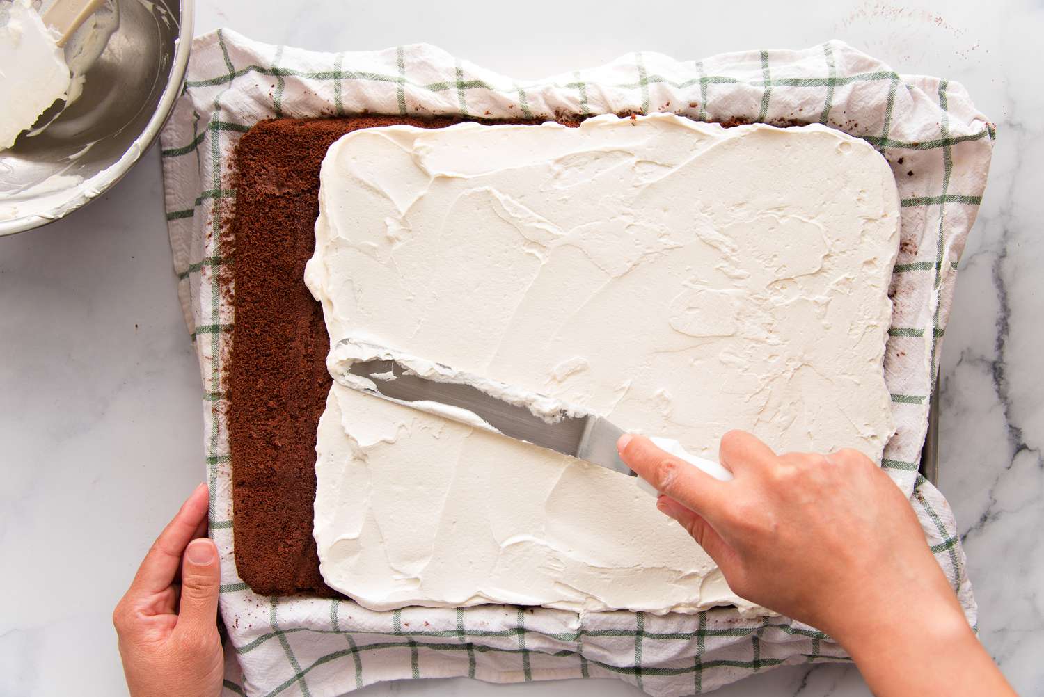 Spreading whipped cream over swiss roll cake.
