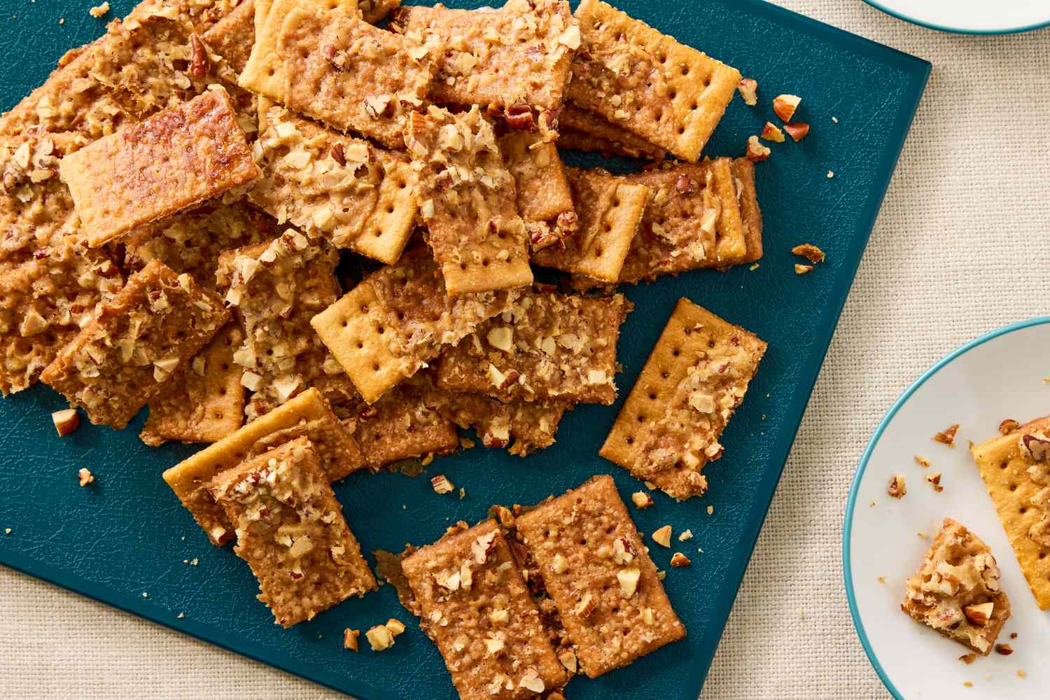 A pile of club crackers topped with a caramelized coating and chopped nuts on a cutting board