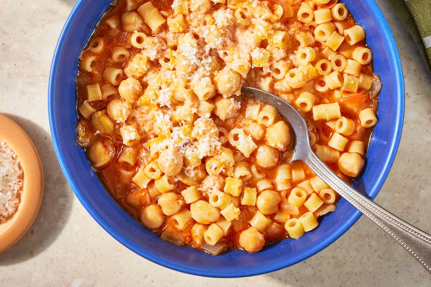 Overhead view of a blue bowl of Pasta e Ceci and a spoon topped with parmesan cheese next to a bowl of parmesan