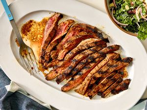 Sliced marinated flank steak on a serving platter with a fork on the side