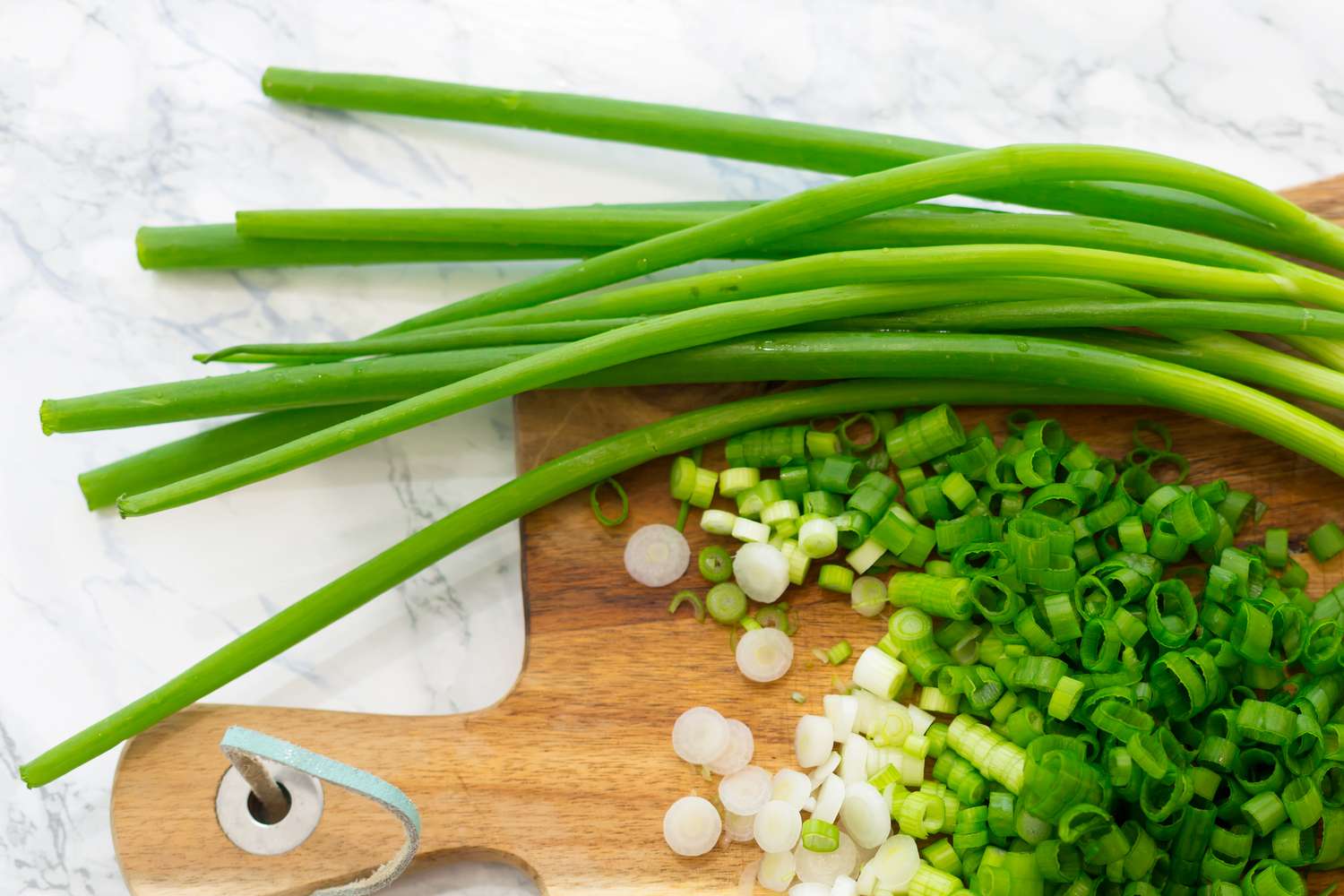 Closeup overhead shot of scallions on a wooden cutting board, part of them sliced up