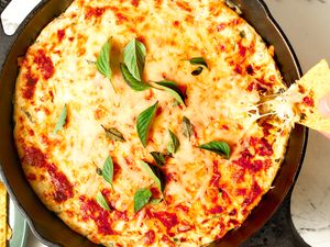 Cast iron skillet with a baked cheese dip garnished with basil and a hand dipping a tortilla chip