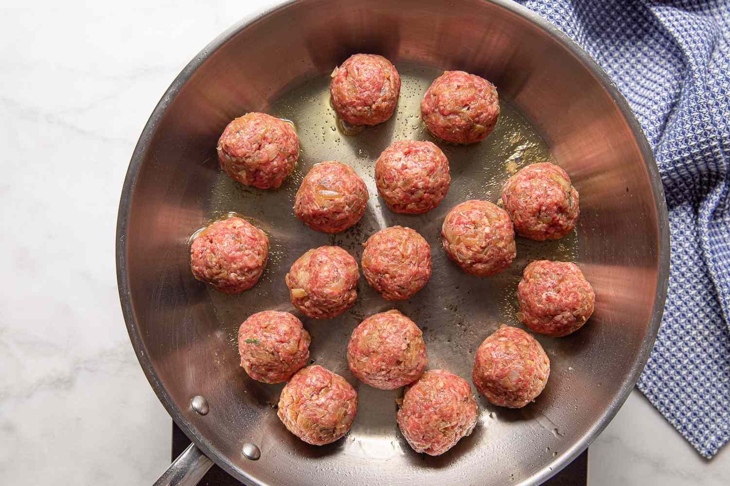 French Onion Meatballs Cooking in a Pan on a Portable Stovetop, and on the Counter Next to It, a Blue Kitchen Towel