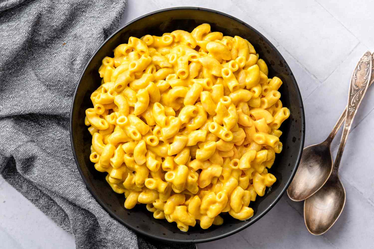 Bowl of Vegan Mac and Cheese Next to Two Spoons and a Table Napkin