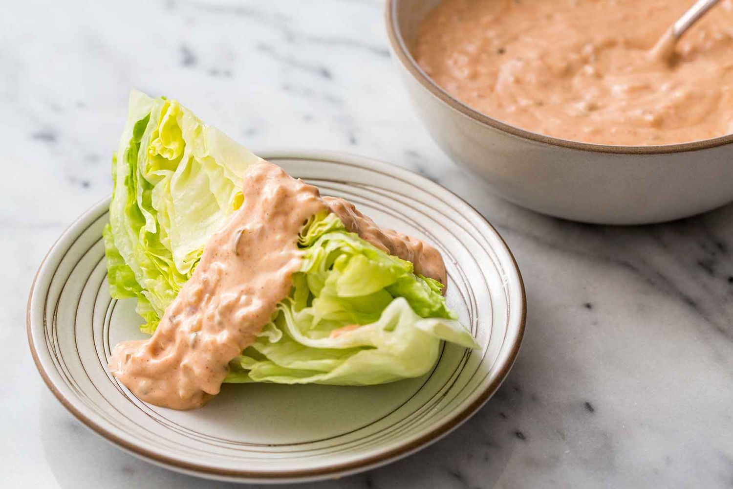 A wedge of iceberg lettuce on a plate with Thousand Island dressing on it