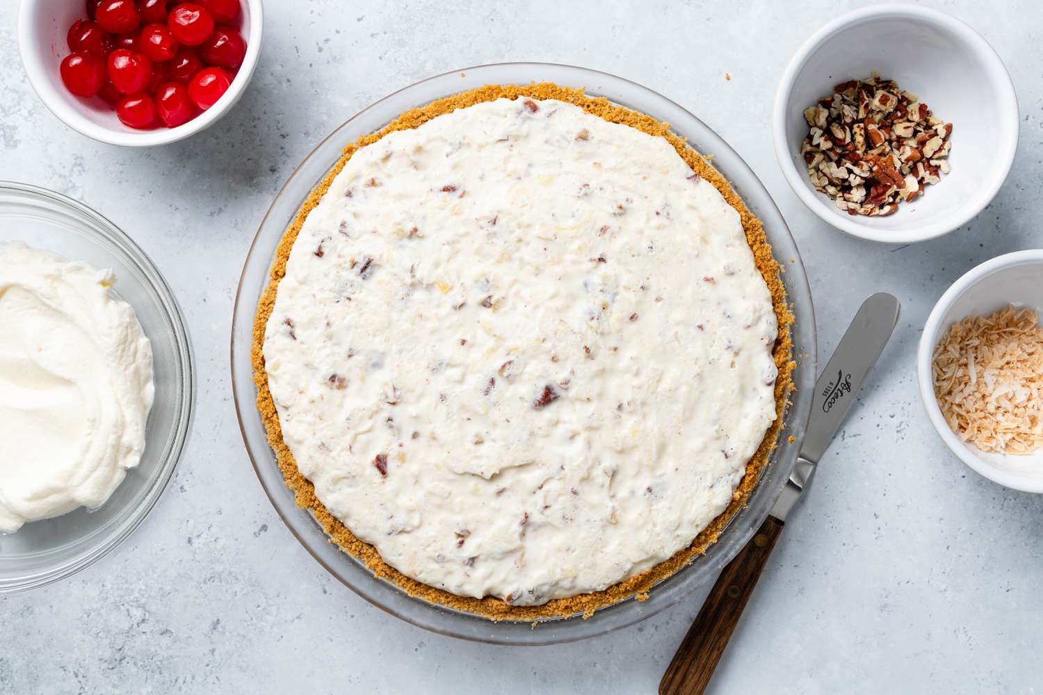 Million Dollar Pie Surrounded by Bowls With Toppings (From L to R: Bowl of Whipped Cream, Bowl of Maraschino Cherries, Bowl of Toasted Chopped Pecans, and Bowl of Toasted Desiccated Coconut)