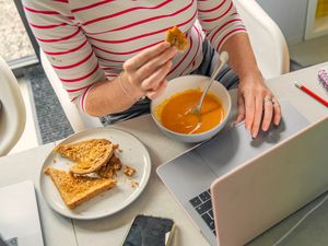 Person eating soup and toast while working on a laptop