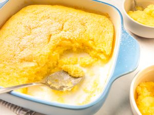 Side angle view of a baking dish with lemon pudding cake with some of the cake scooped out in two small bowls