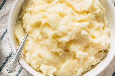 Overhead view of a white bowl of creamy mashed potatoes with a serving spoon