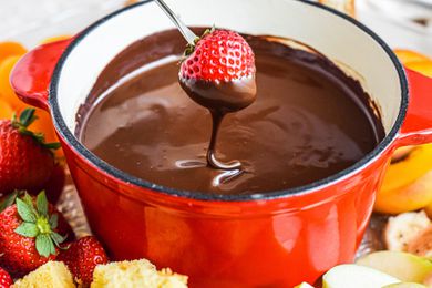 Dipping a strawberry into fondue chocolate with other dippers surrounding.