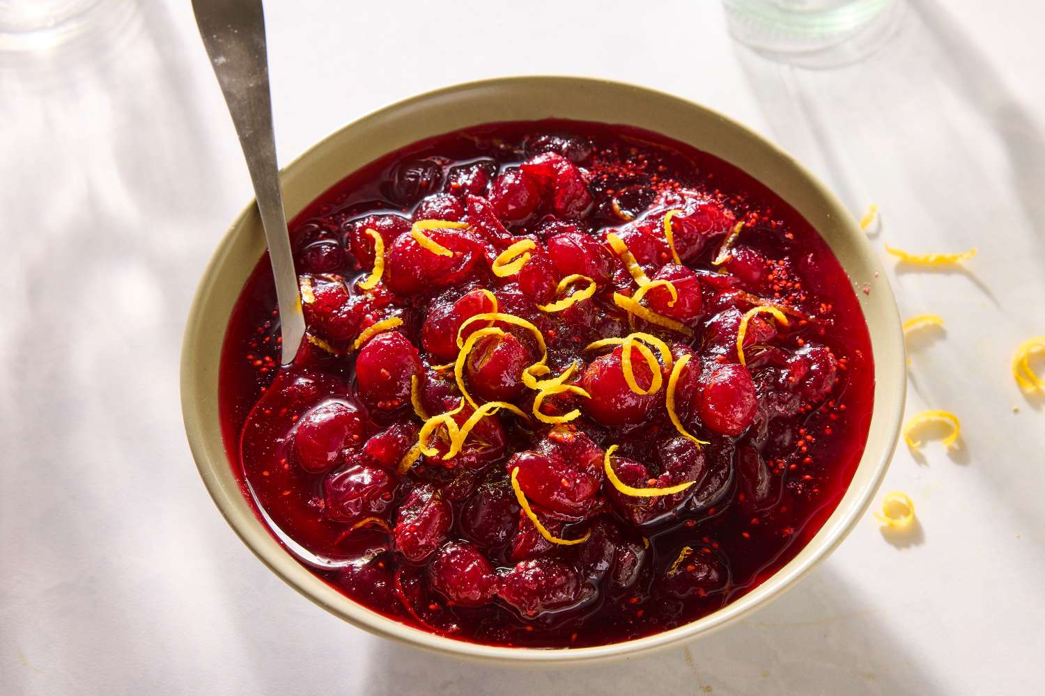 Bowl of cranberry sauce garnished with citrus zest, with a spoon