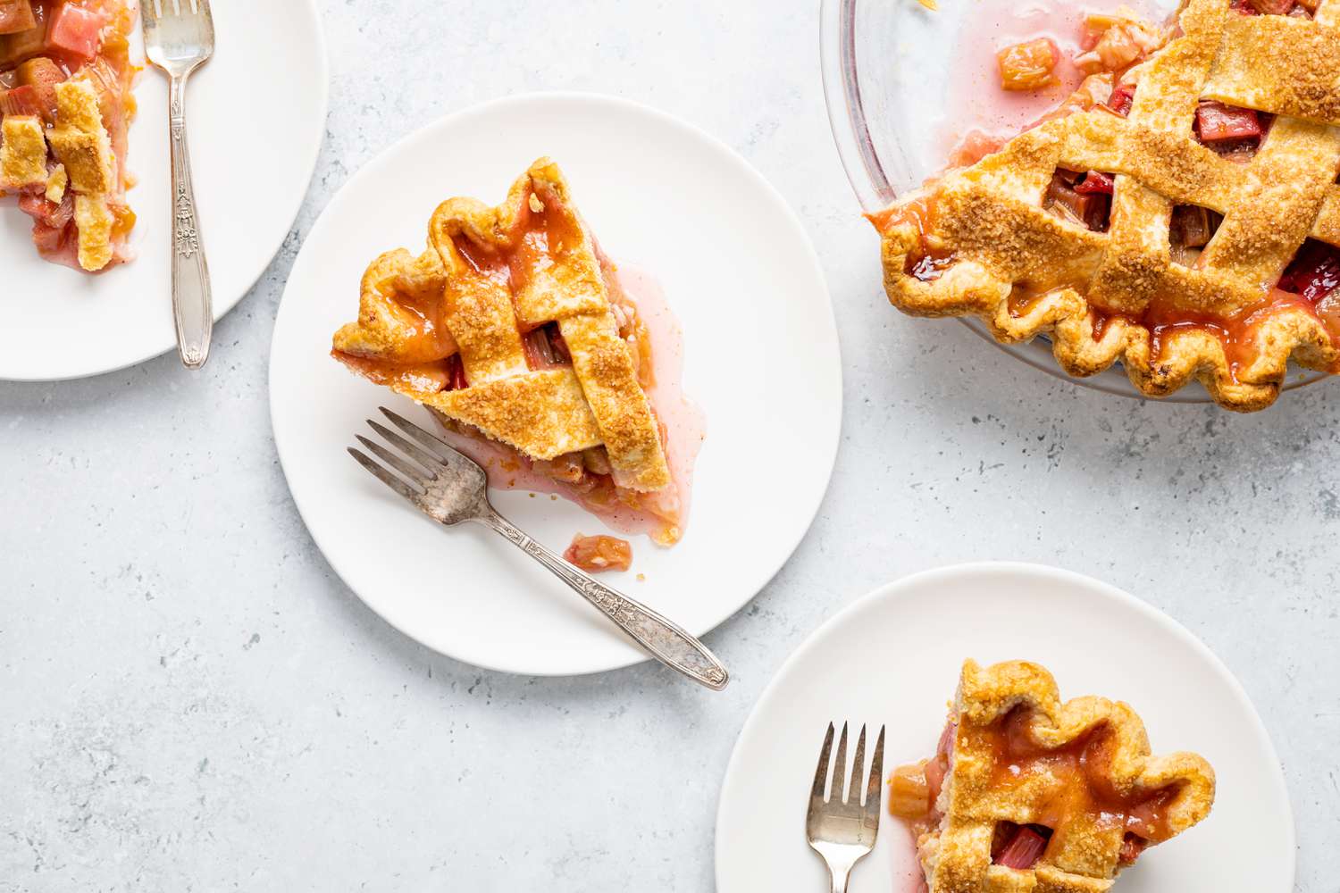 Slices of Rhubarb Pie on a Plate with a Fork Surrounded by More Plates and a Pie Dish with Pie