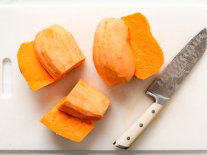 Overhead view of a white cutting board with a large knife and two sliced sweet potatoes