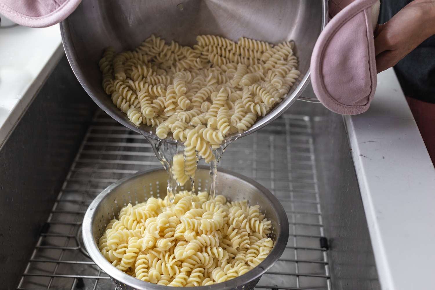 Pouring spiral noodles into a strainer to make pesto pasta salad.