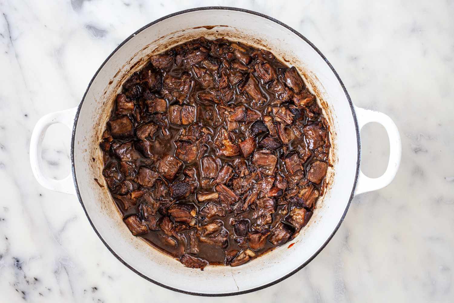 Overhead view of braised oxtails in a dutch oven.