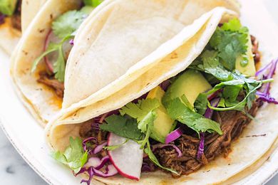 Three tacos filled with pulled pork cabbage and cilantro on a white plate