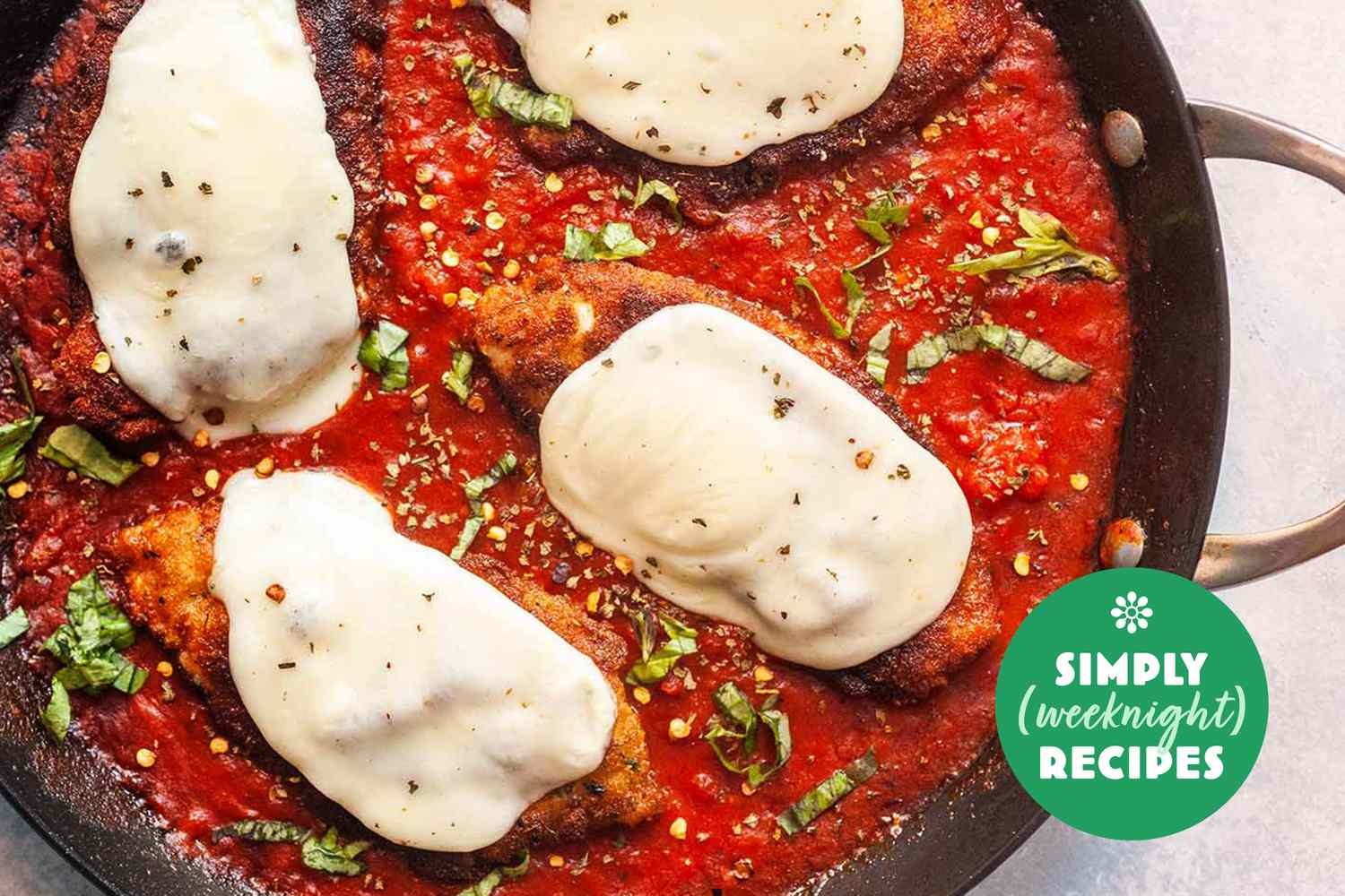 Chicken Parmesan with melted cheese in a skillet with tomato sauce and basil garnish