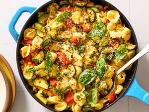 A skillet with tortellini, zucchini, tomatoes, basil, and cheese