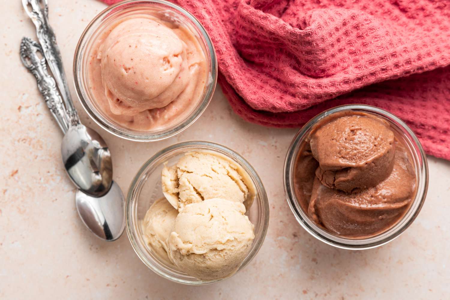 Banana Nice Cream Variations in Three Small Bowls Next to Two Spoons and a Kitchen Towel