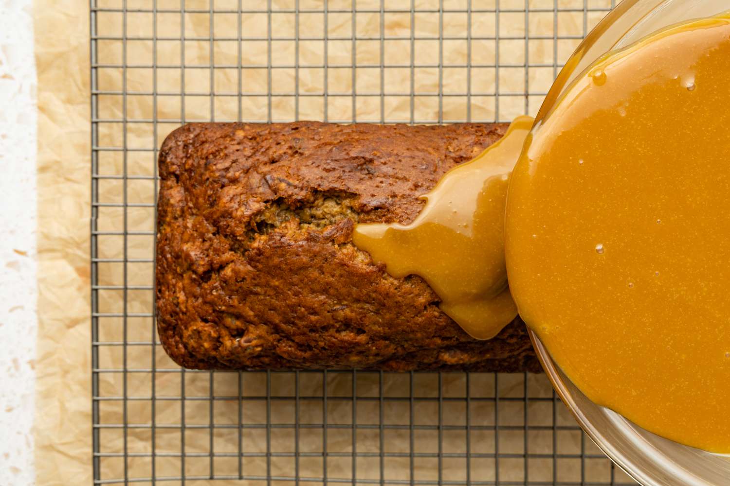 Caramelized White Chocolate Sorghum Glaze Poured Onto Banana Pecan Bread on a Wire Cooling Rack With Parchment Paper Under It
