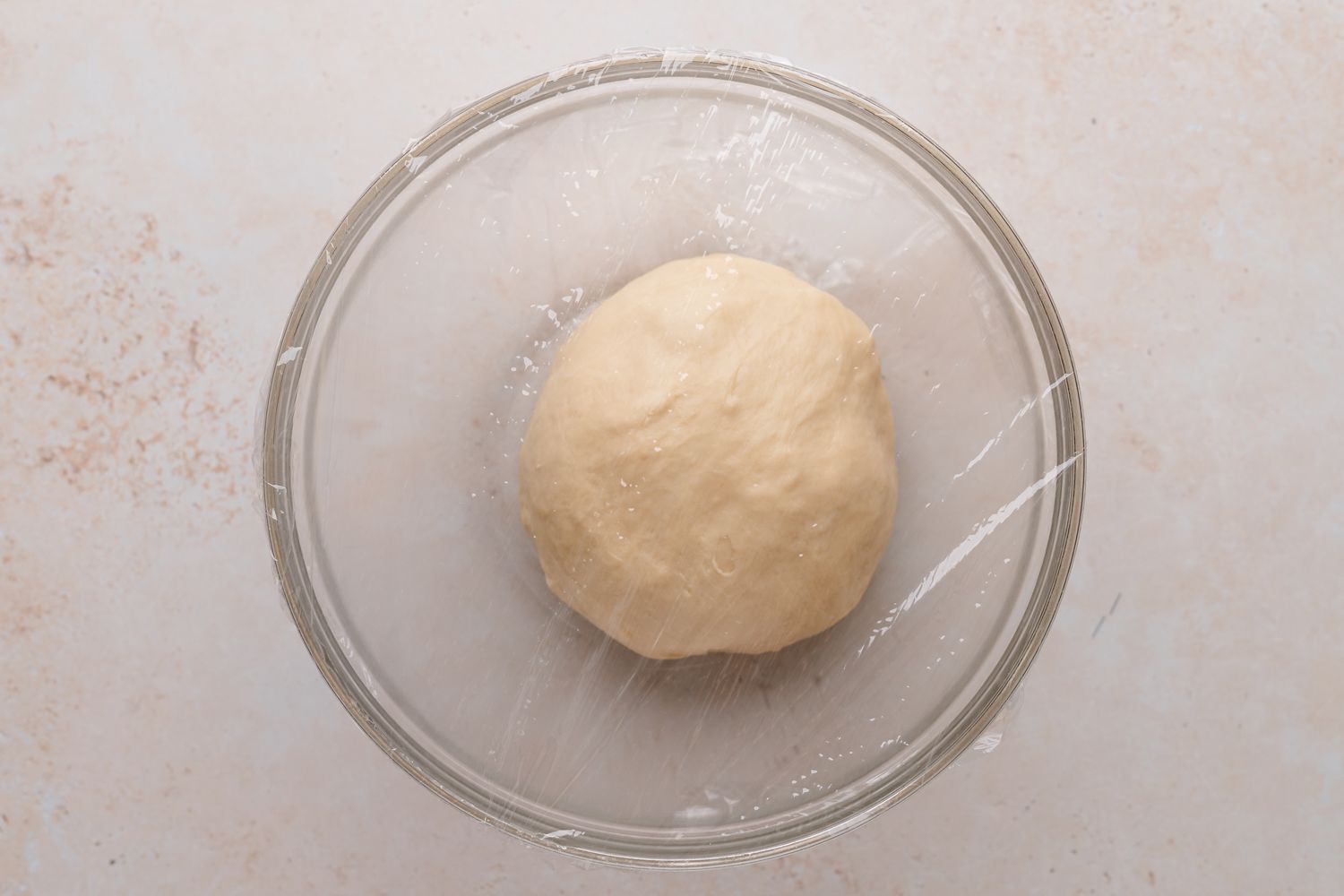 Braided chocolate babka dough rising in a glass bowl.