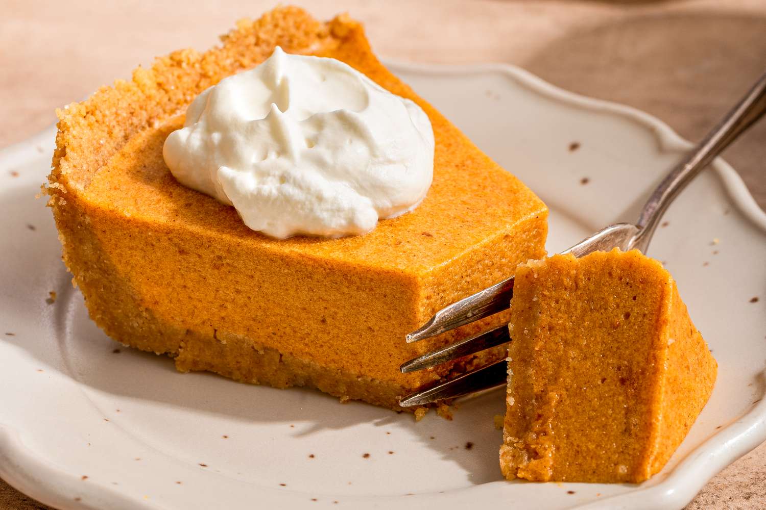 A slice of pumpkin pie with whipped cream on a plate a fork holding a small piece