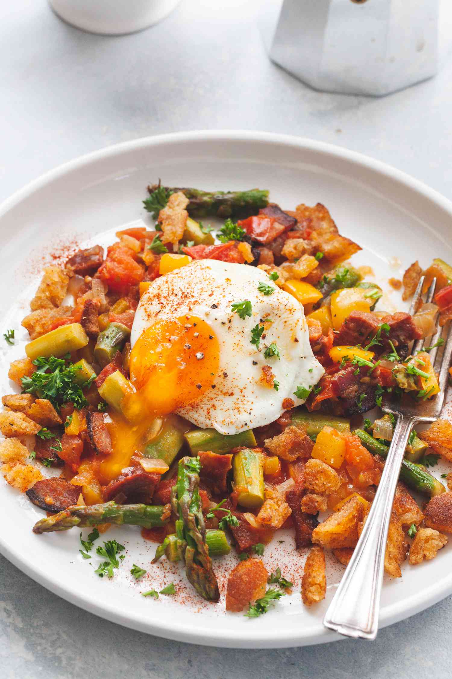 A white plate with Spanish Style Migas with Asparagus, Chorizo, Bacon, and Eggs.
