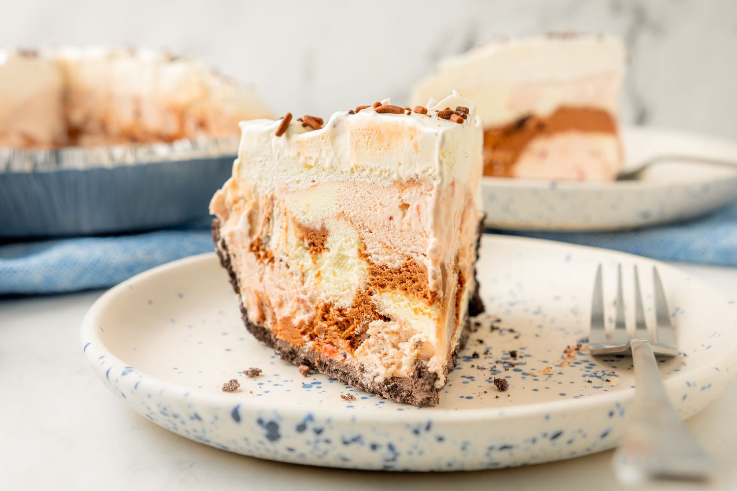 A slice of layered ice cream pie on a speckled plate with a fork beside it