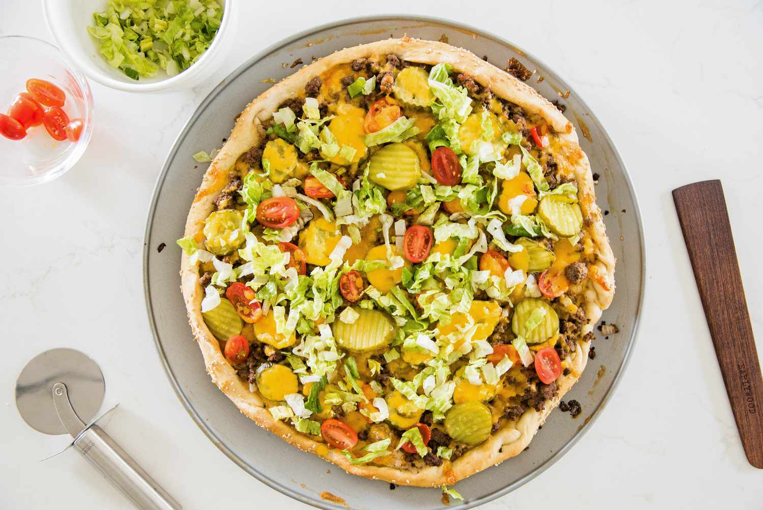 Cheeseburger Pizza Topped with More Pickles, More Cherry Tomatoes, and Shredded Lettuce