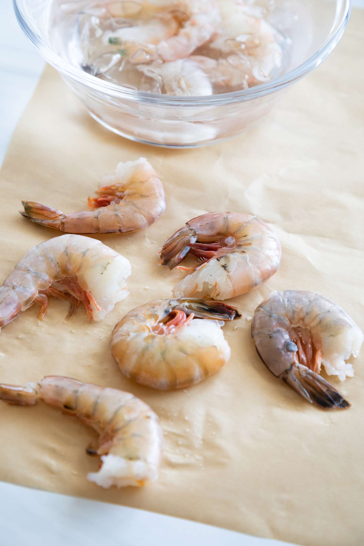 Side view of devein shrimp on a cutting board with the shells in a small bowl next to them.