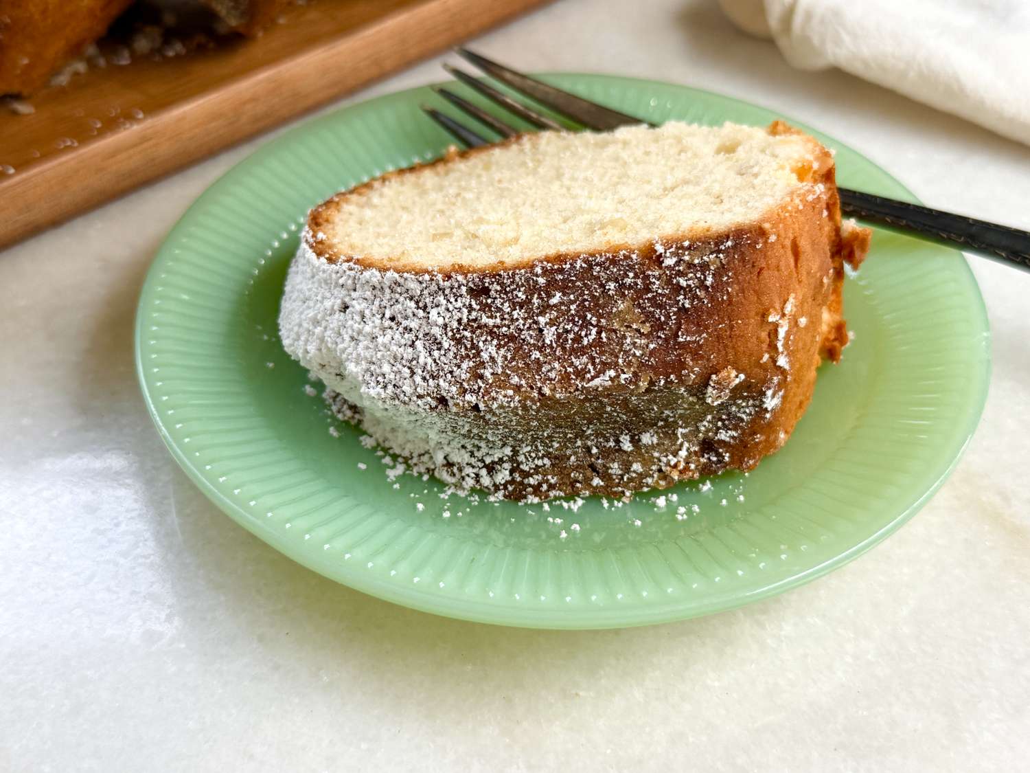 Slice of almond cake on a green plate with a fork