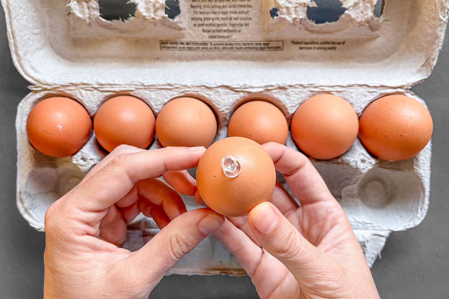 Hands holding an egg with a push pin pressed into the end
