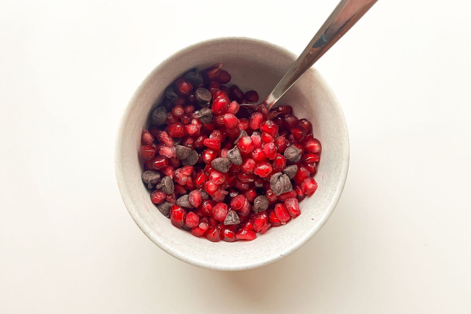 A bowl containing pomegranate seeds mixed with chocolate chips a spoon is placed inside