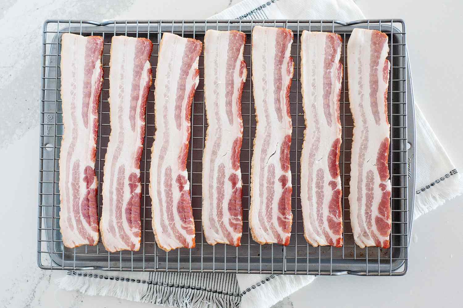 How to cook bacon in the oven by setting it on a cooling rack over a sheet pan.