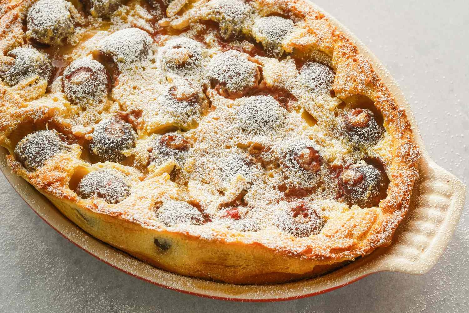 Baked cherry clafoutis in an oval dish, topped with powdered sugar