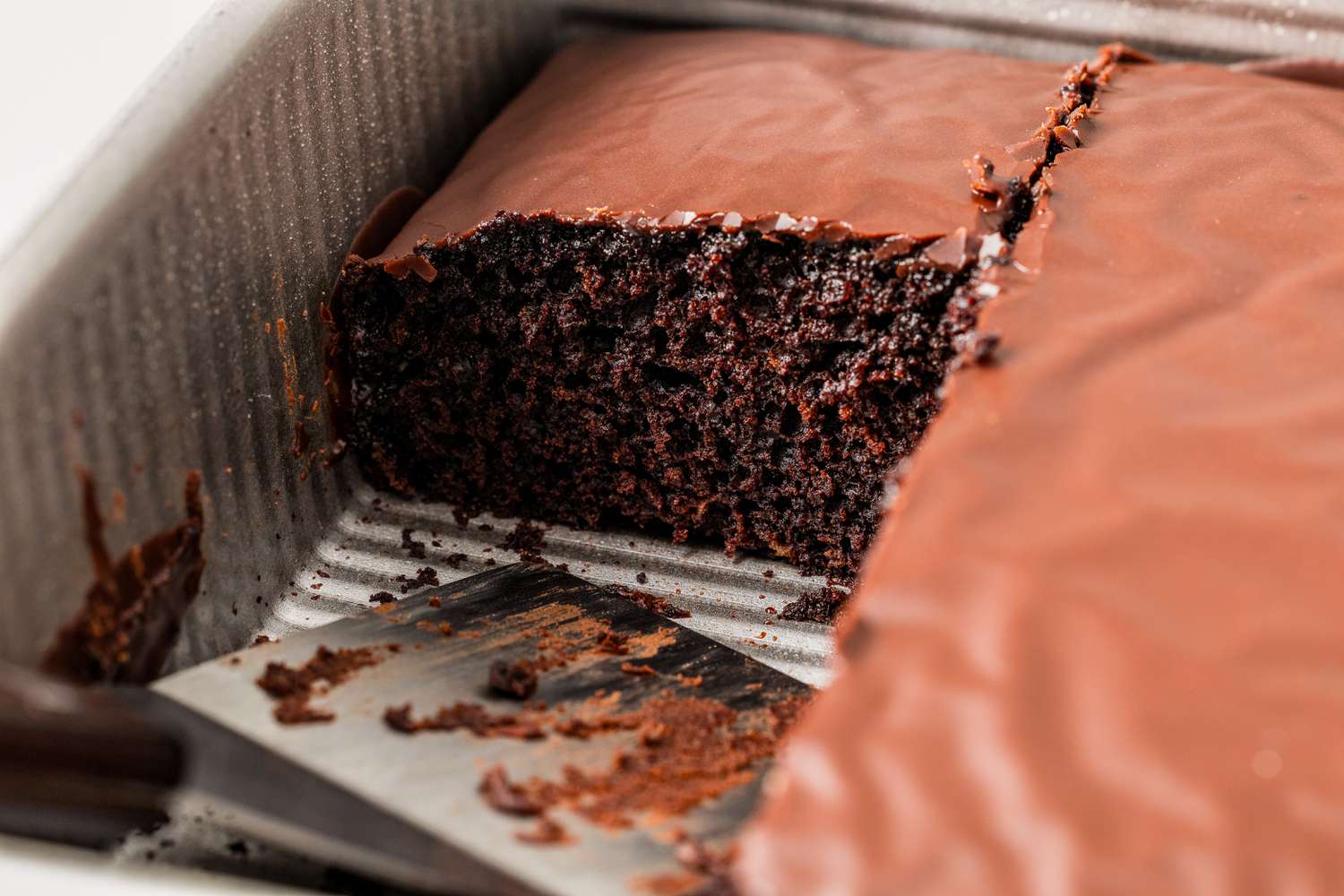 Chocolate Depression cake in a baking pan with a couple of slices taken out and a spatula