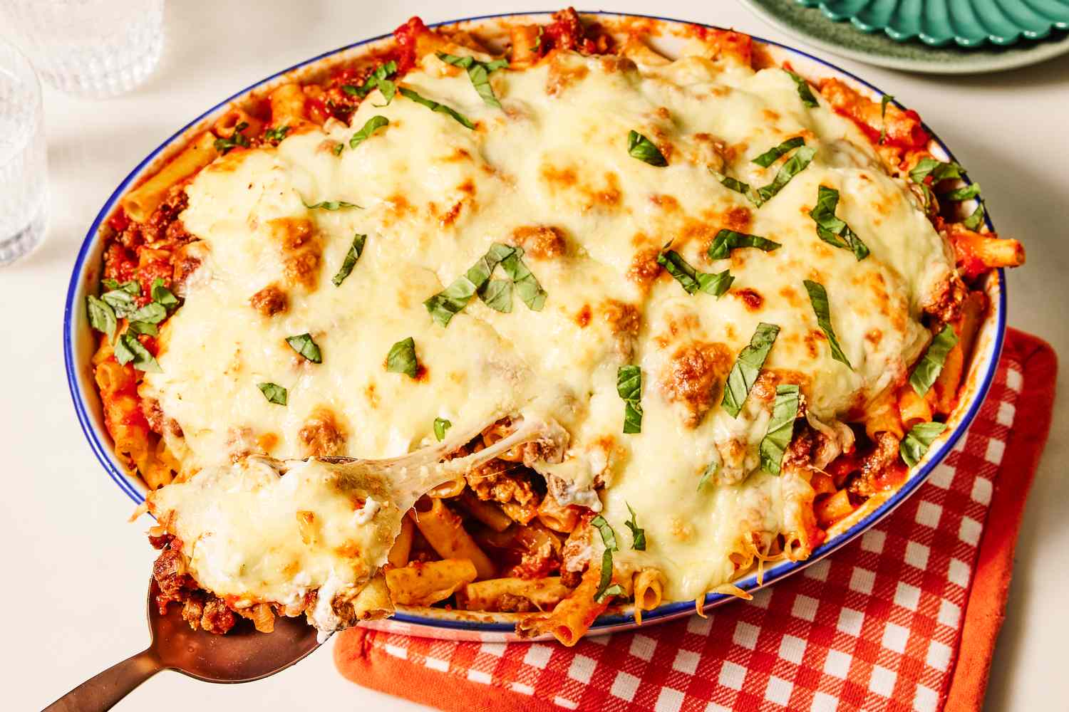 Baked ziti casserole with melted cheese and chopped basil in a dish with a serving spoon