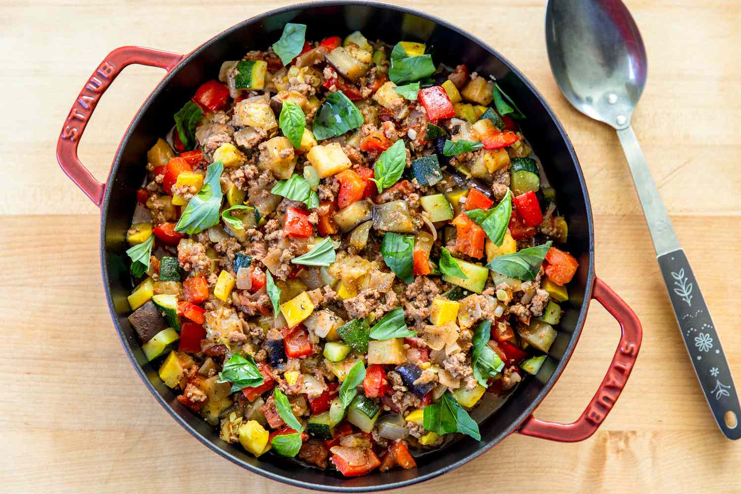 A skillet containing a cooked dish of diced vegetables and ground beef, garnished with fresh basil