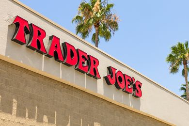 Trader Joes store sign on an exterior wall with palm trees in the background