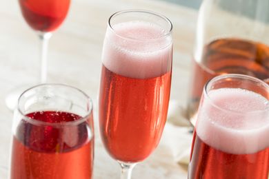 Fizzy pink cocktails in champagne flutes on a light wooden surface