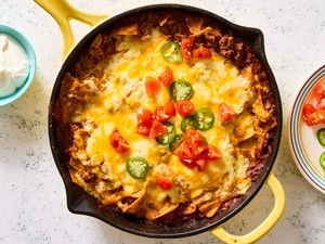 Beef enchilada skillet topped with melted cheese, chopped tomatoes, and jalapenos