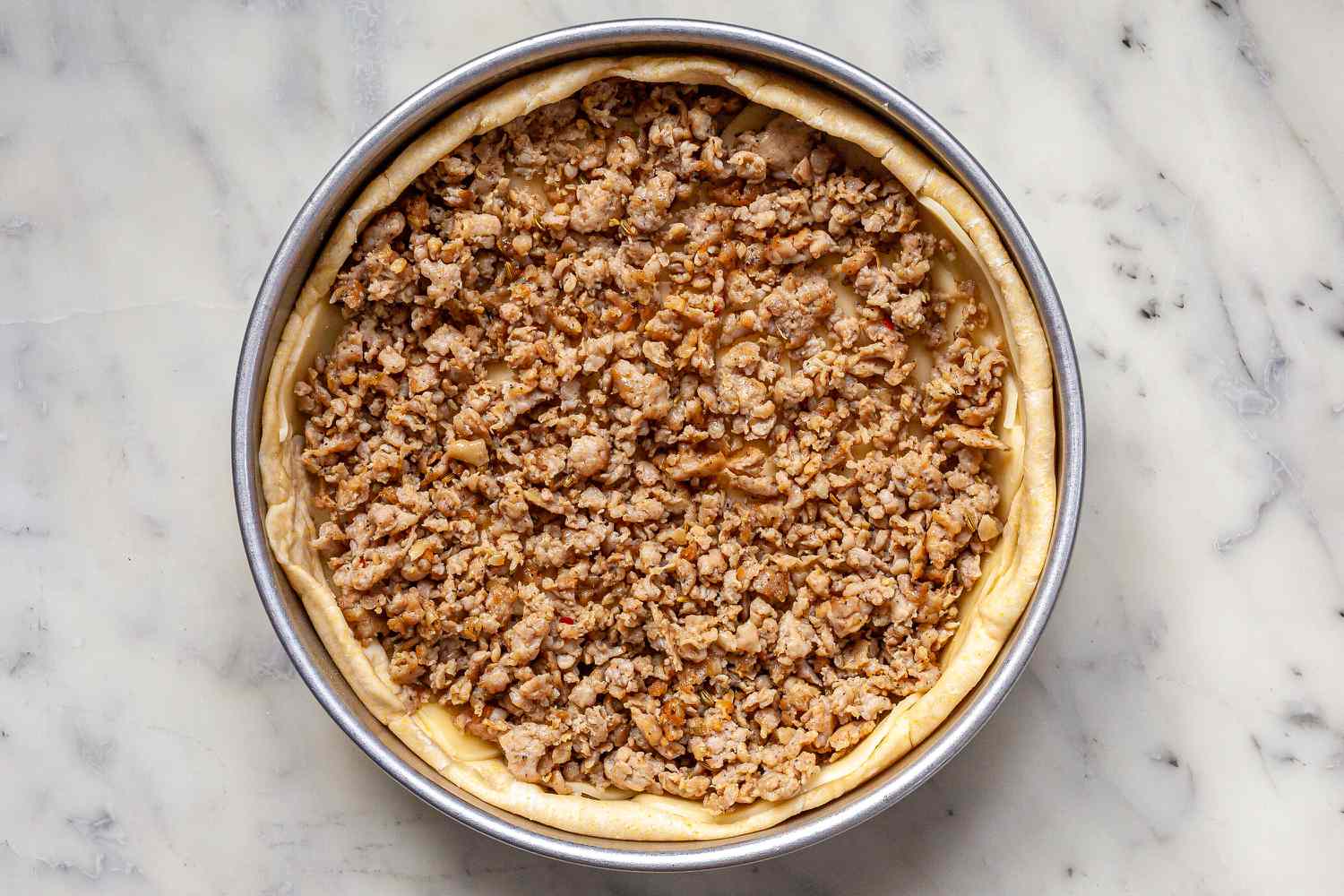 Sausage spread onto crust for Chicago-Style Deep Dish Pizza.