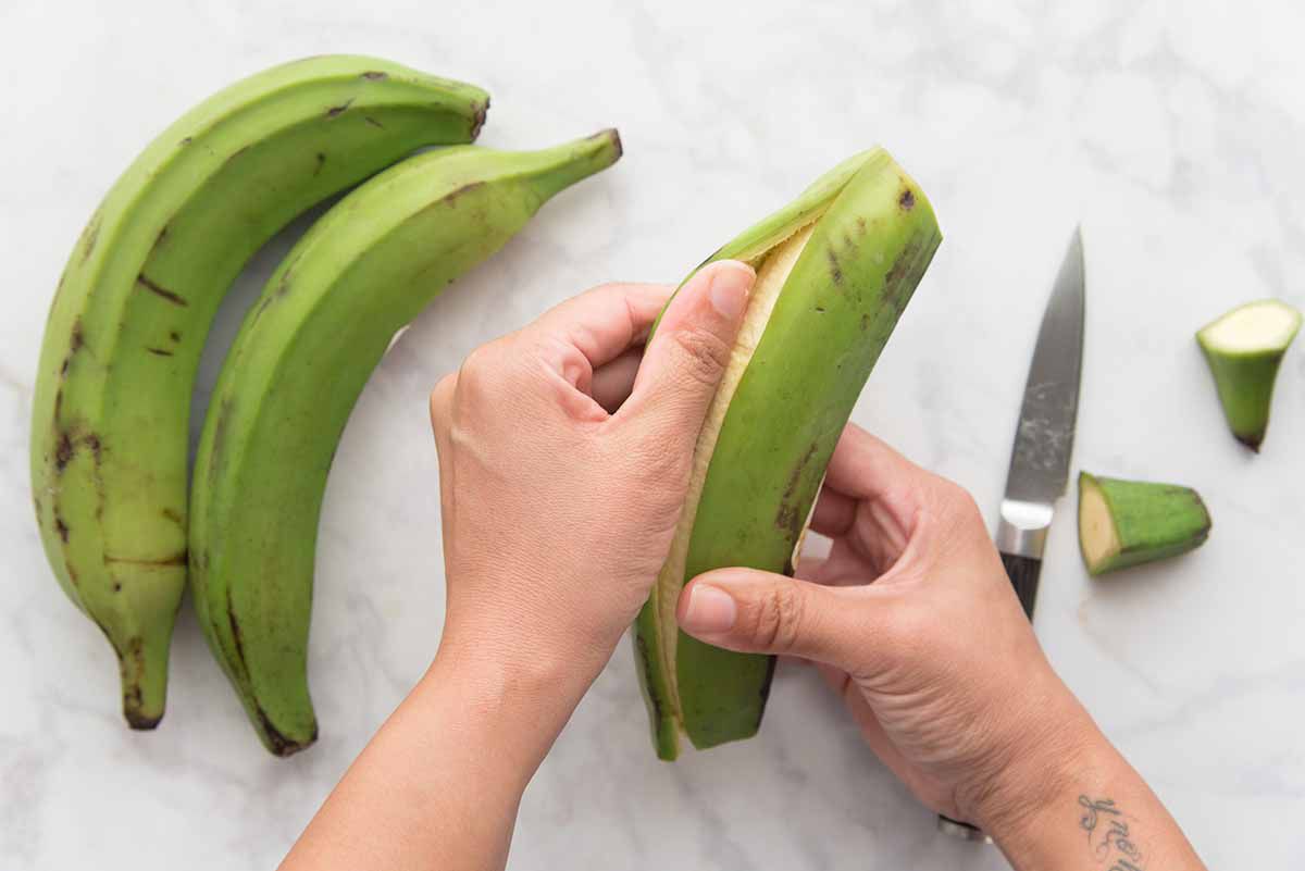 Person peeling a green plantain