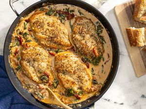 creamy tuscan chicken in a pot next to sliced bread on a wooden board