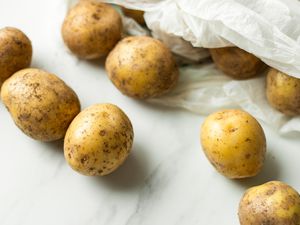 Overhead view of potatoes inside and outside a shopping bag on a marble countertop