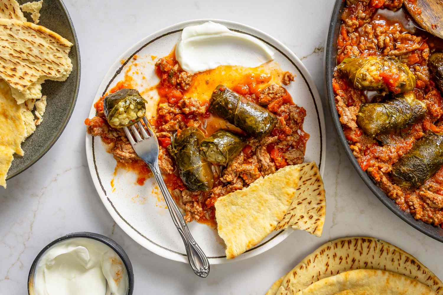 A plate of dolma and beef mixture topped with a dollop of yogurt, served with pita bread