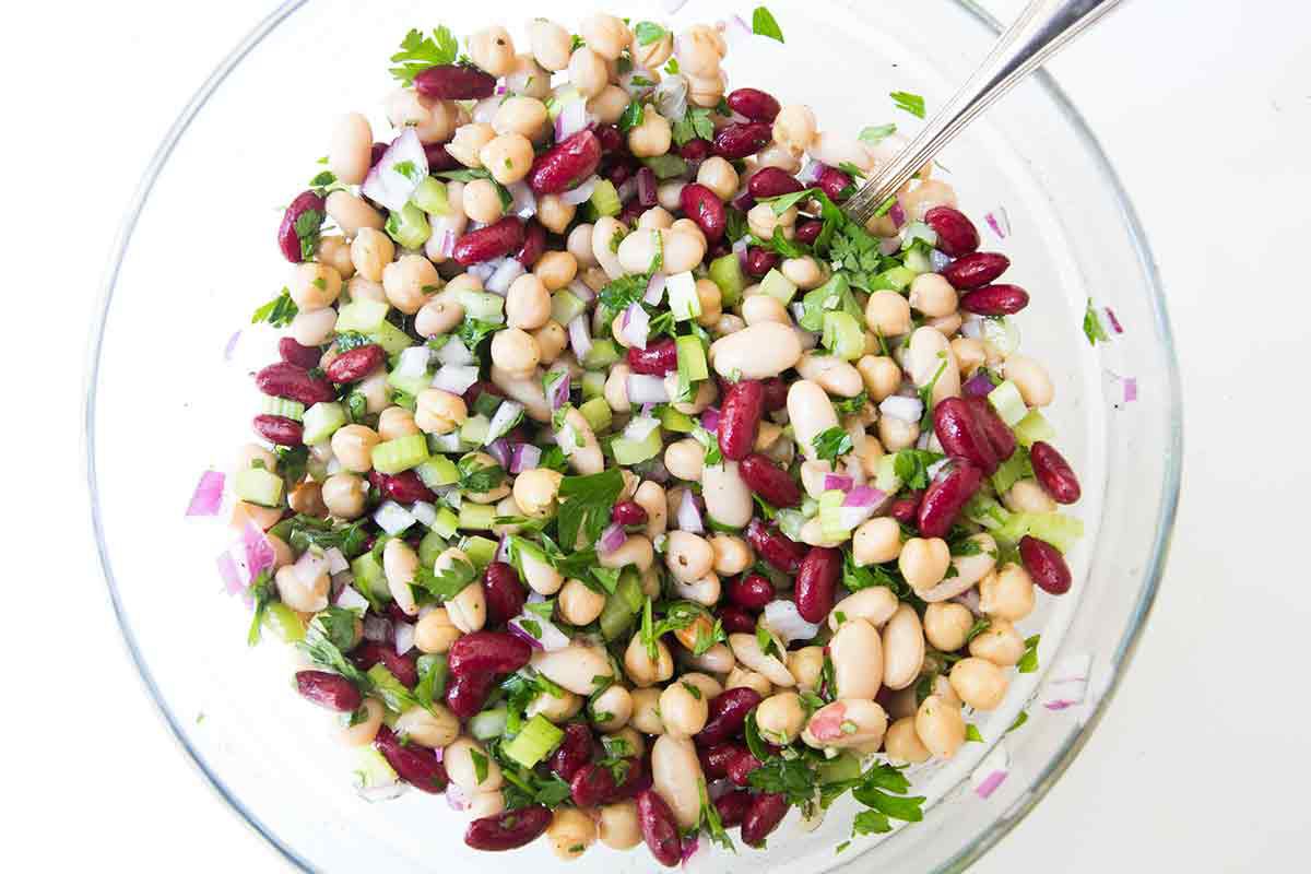 Three bean salad ingredients being stirred together in a glass bowl 