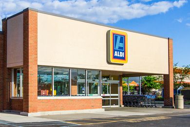 Ground level view of an Aldi grocery store front, front doors, windows and shopping carts with a blue sky and a few clouds