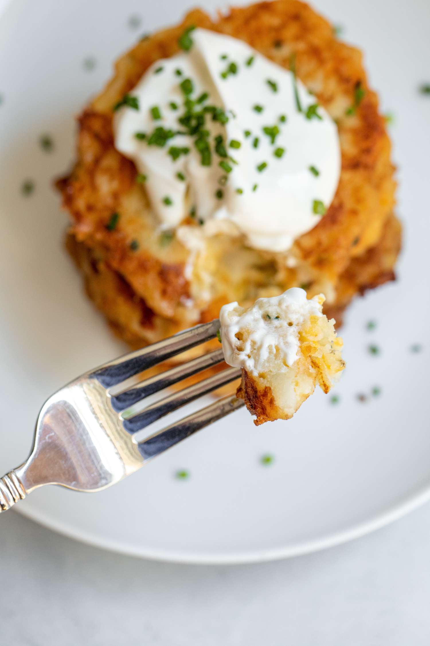 Cheesy mashed potato pancakes with a bite on a fork held above the plate.