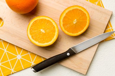 Overhead view of a sliced up orange and a knife on a wooden cutting board